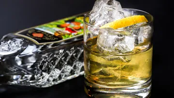 Glass with ice and lemon beside bottle.