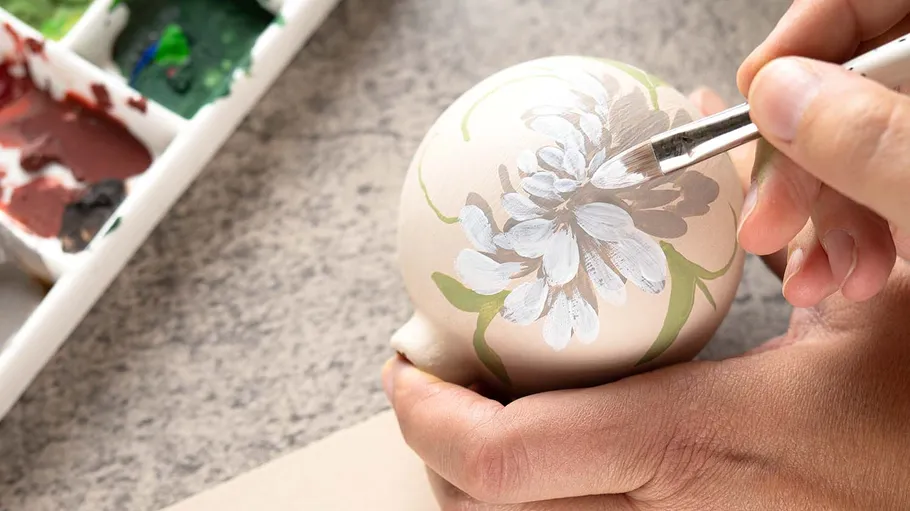 Person painting flower on round object.