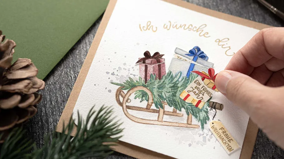 Hand holding card with festive sleigh illustration.