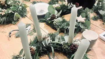Vier Kerzen auf dekorativen Kränzen auf Tisch.