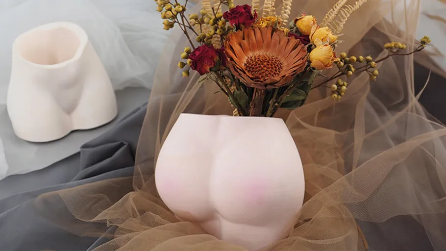 Torsoförmige Vasen mit Blumen auf Stoff drapiert.