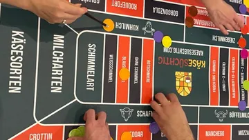 Hände platzieren Spielsteine auf einem Käsebrettspiel.