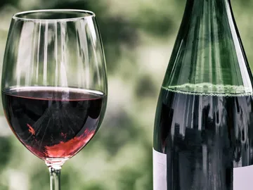 Weinglas mit Rotwein neben einer grünen Flasche.