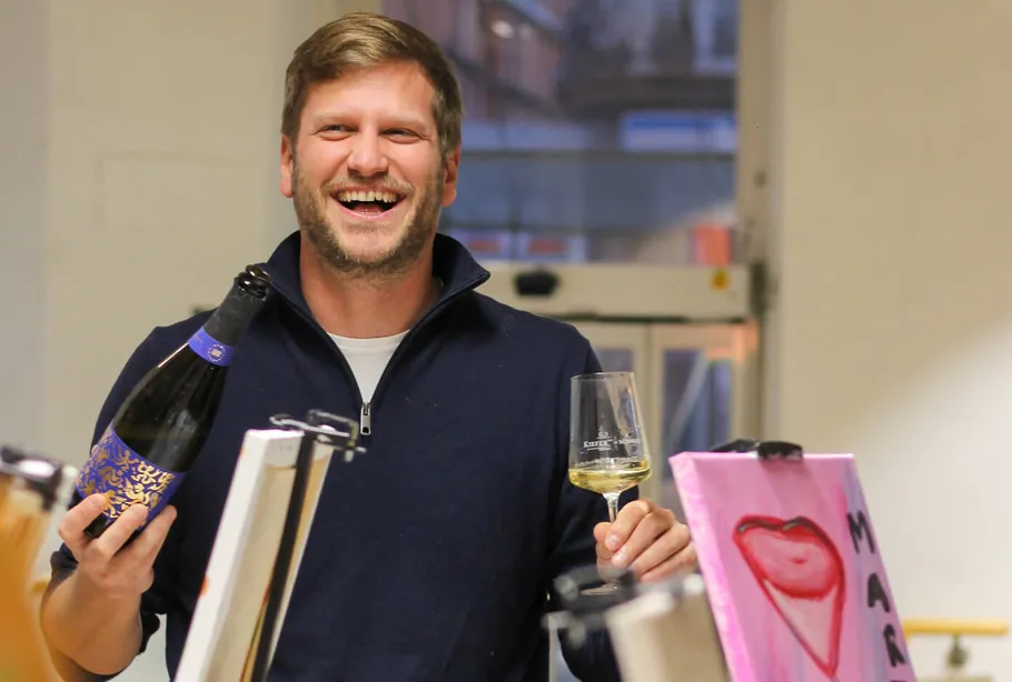 Mann lacht, hält Wein, Innenraum.