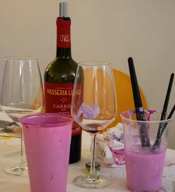Wine bottle, glasses, and paintbrushes on table.