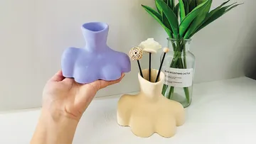 Purple vase held next to beige vase with decoration.