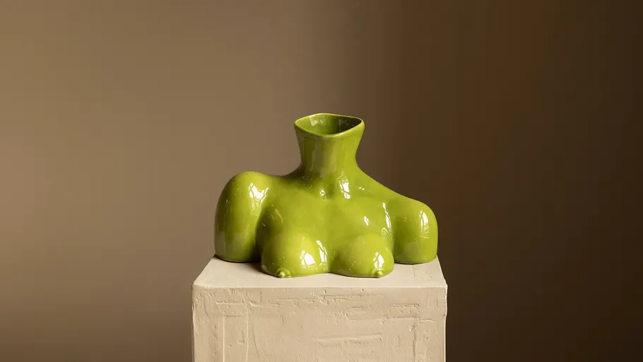 Grüne Keramikvase auf Sockel im Innenraum.