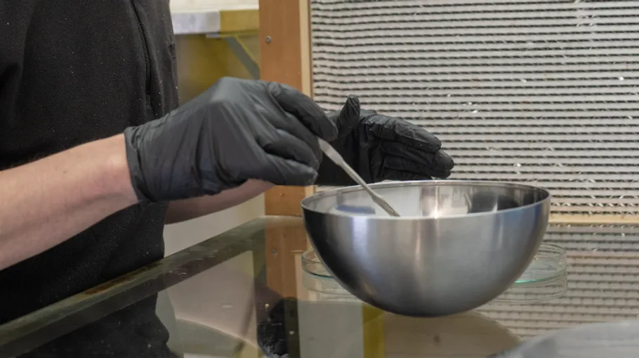 Gloved hands stirring mix in metal bowl.