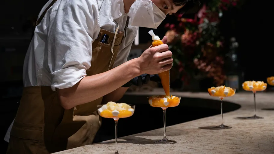 Chef piping cream onto desserts on counter.
