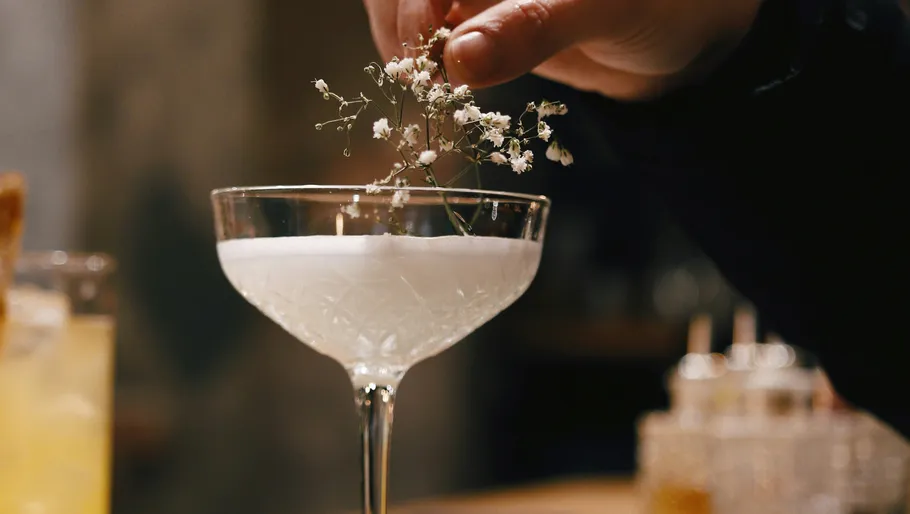 Hand garniert einen Cocktail mit Blumen.