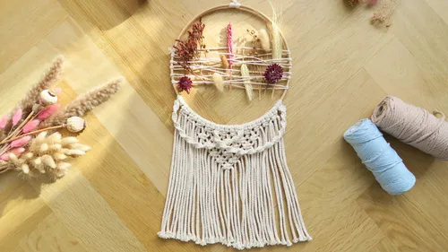 Macramé wall hanging with dried flowers on wood floor.