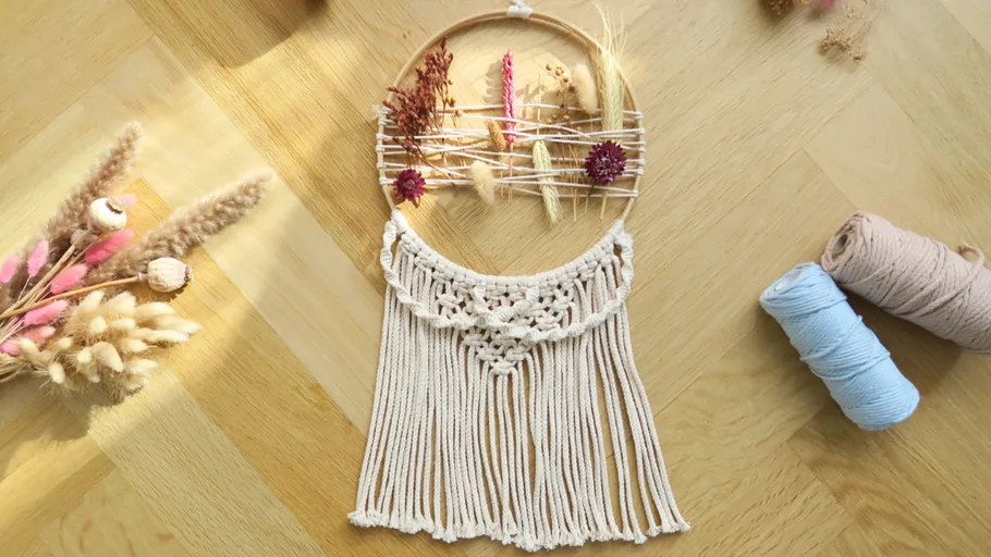 Macramé wall hanging with dried flowers on wood floor.