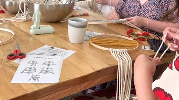 People crafting macramé at a wooden table.