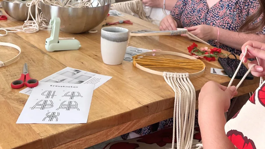 People crafting macramé at a wooden table.