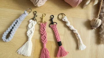 Five macrame keychains on wooden surface.