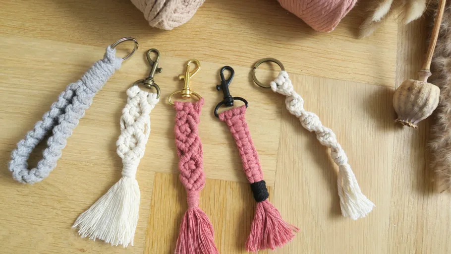 Five macrame keychains on wooden surface.