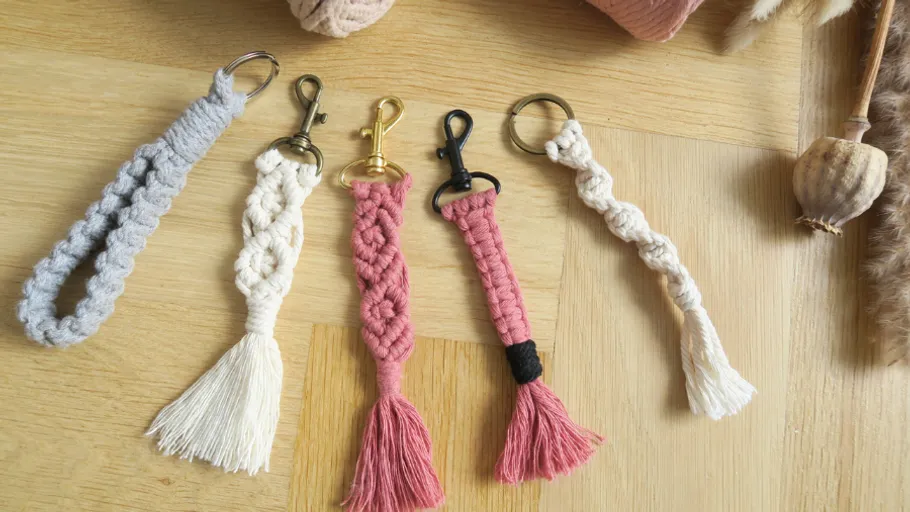 Five macrame keychains on wooden surface.