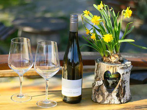 Weißweinflasche steht neben Gläsern und Blumenvase.