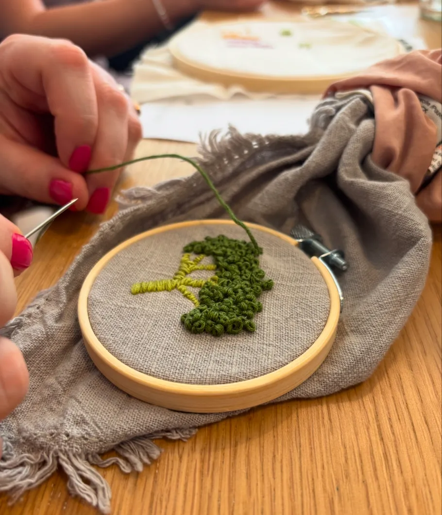Hands embroidering green design on wooden hoop.