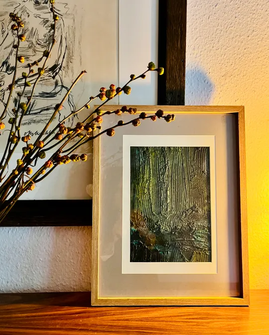 Gerahmtes abstraktes Gemälde neben Zweigen, warm beleuchtet.