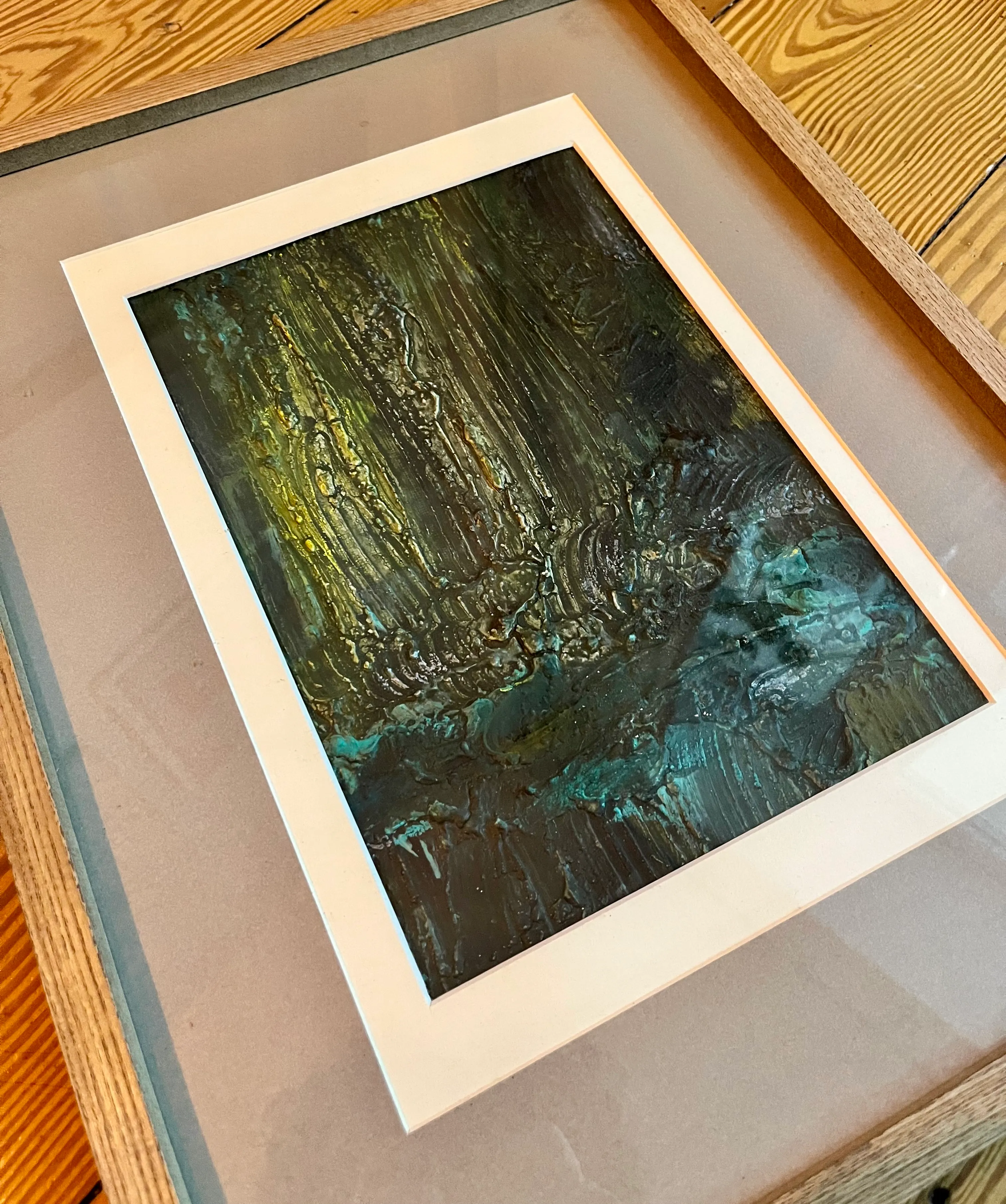 Abstraktes Gemälde in Holzrahmen, auf einem Tisch.