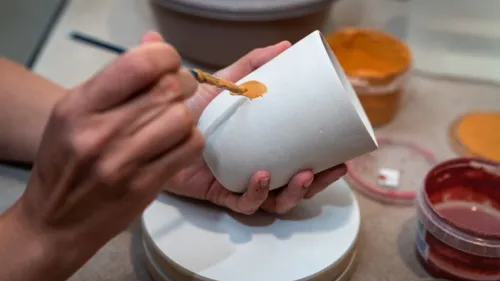 Person bemalt keramische Tasse mit orangefarbener Farbe.
