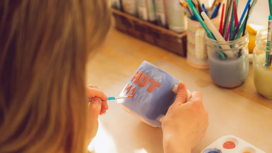 Person malt eine Tasse mit 'HOT MAMA' Schrift.