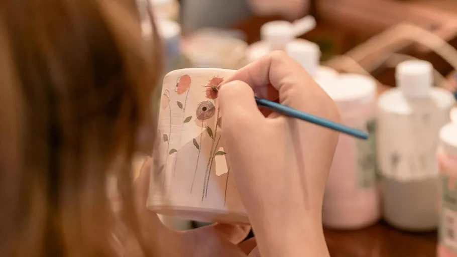 Person painting flowers on ceramic mug.