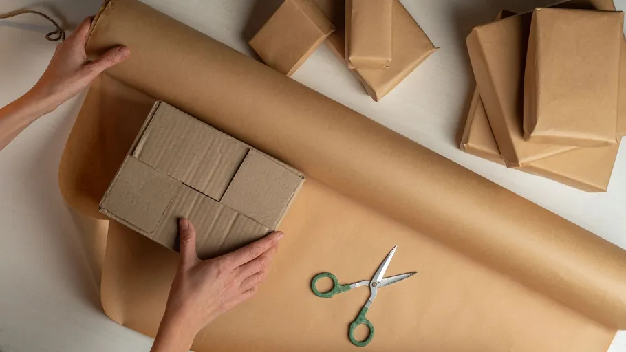 Hände verpacken Pakete in braunem Papier.
