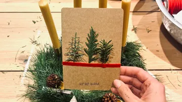 Hand holding card with tree design, festive setting.