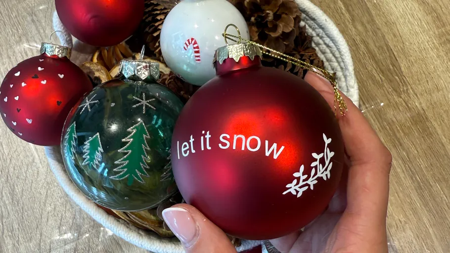 Hand hält roten Ornament, Korb mit Weihnachtsdekorationen.