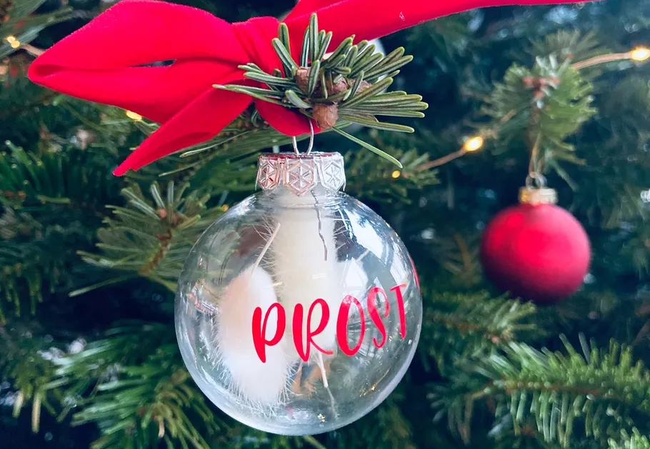 Glaskugel mit 'PROST' hängt am Weihnachtsbaum.