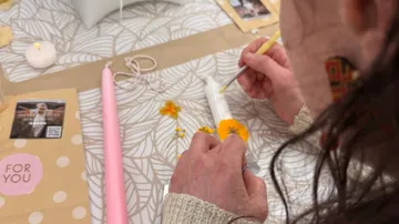 Person verziert Kerze mit gelben Blumen.