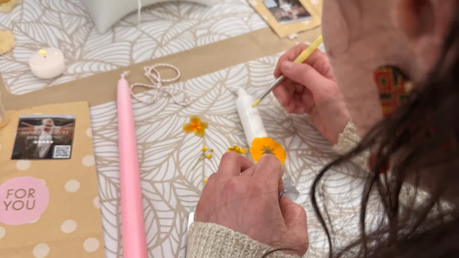 Person decorates candle with yellow flowers.