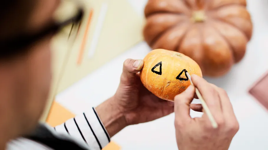 Person drawing on small pumpkin face indoors.