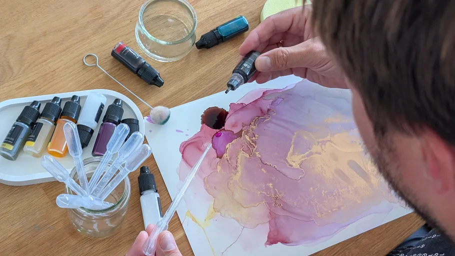 Person erstellt Kunst mit bunten Tinten auf Papier.