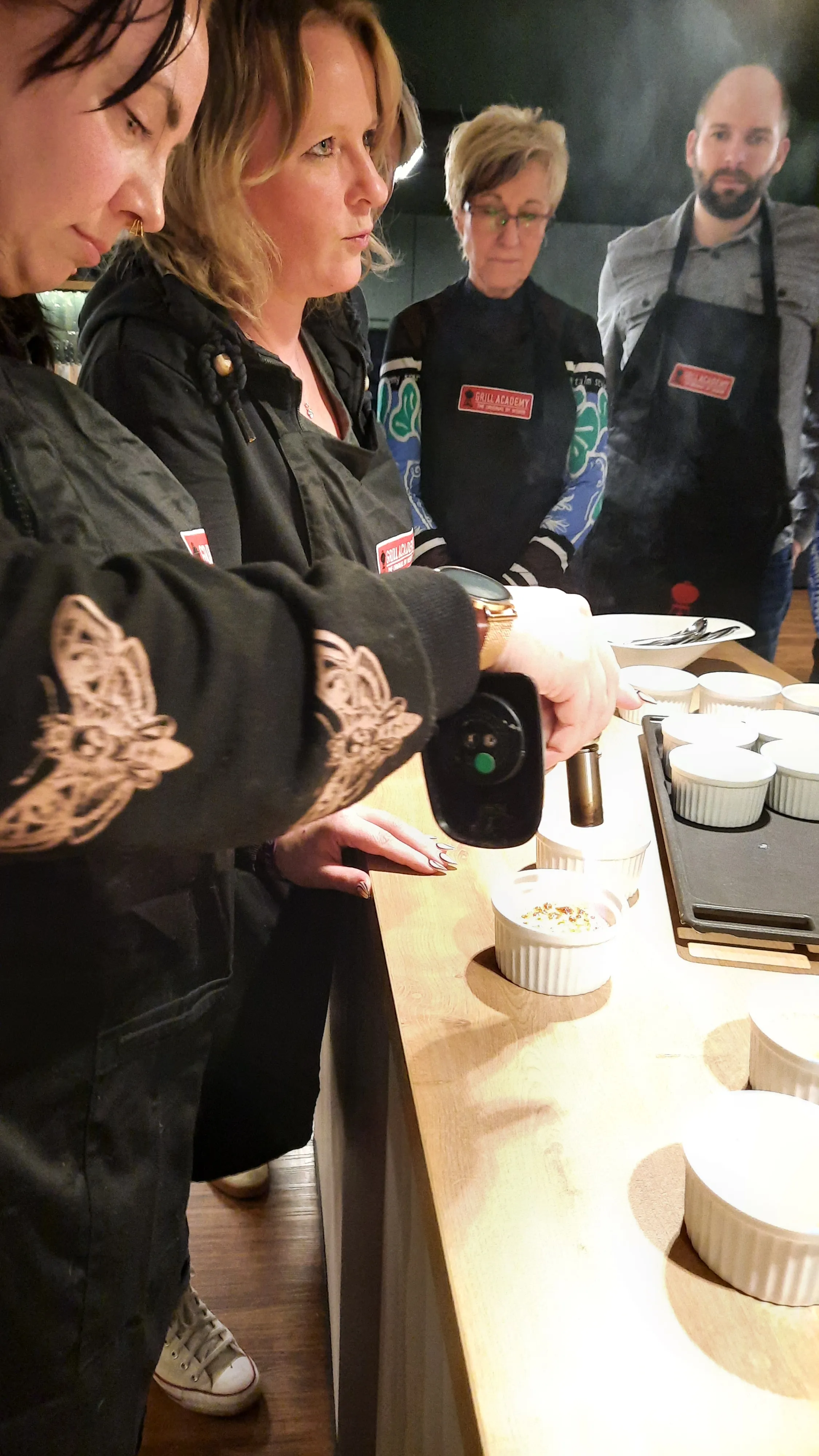 Person verwendet Brenner auf Essen, andere schauen zu.