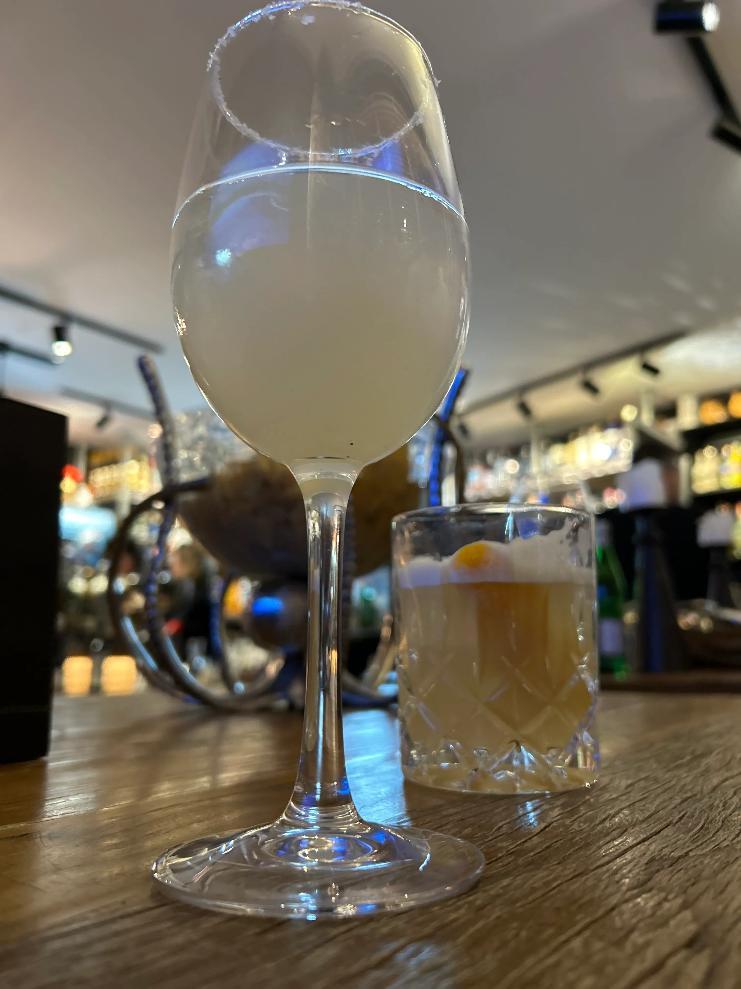 Two cocktails on a wooden bar counter.