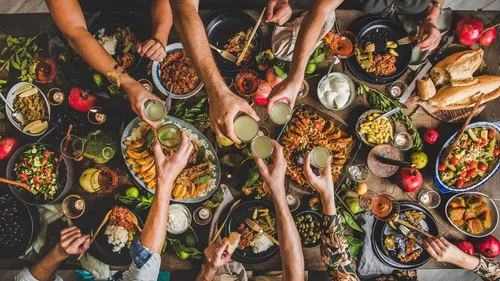 Menschen stoßen an einem bunten Esstisch an.