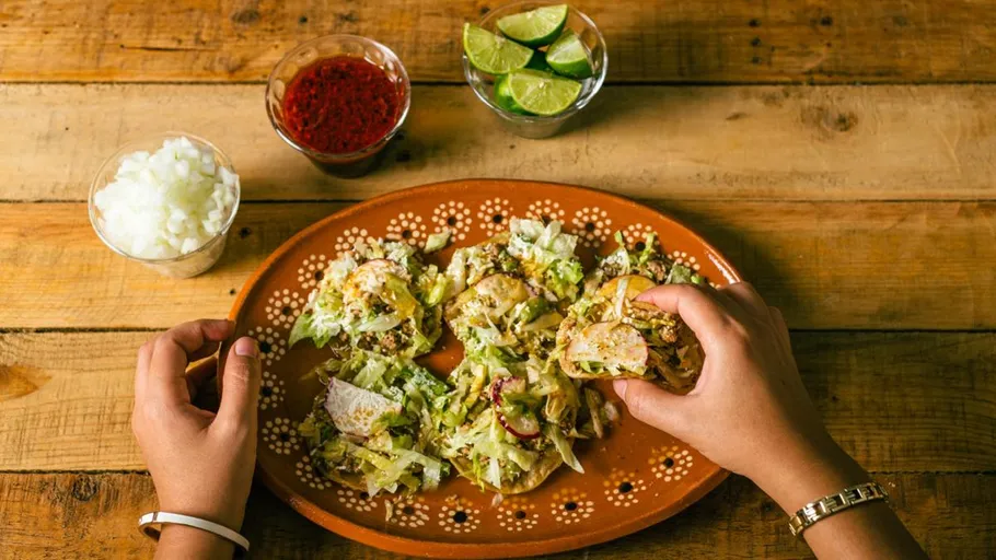 Hands holding tacos on a wooden table.