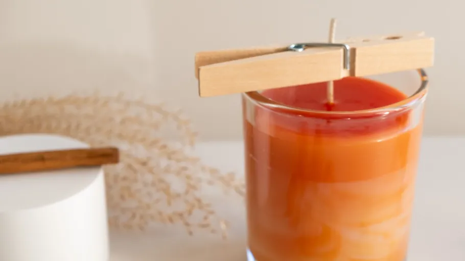 Orange candle with clothespin, neutral background.
