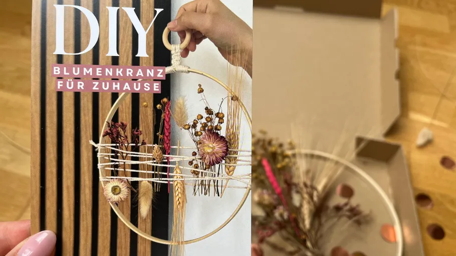 Hand hält DIY-Blumenkranz in Innenraum.