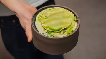 Hand hält Schüssel mit geschichtetem grünen Essen.
