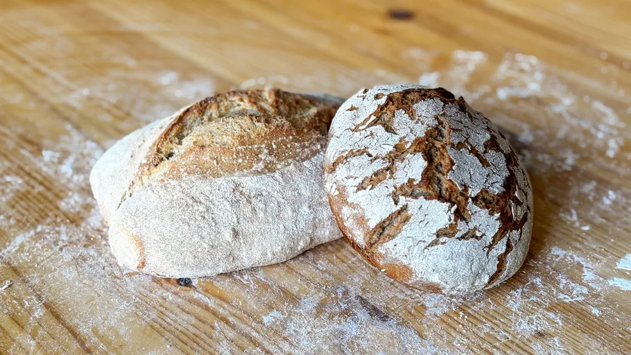 Two loaves of bread on wooden table.