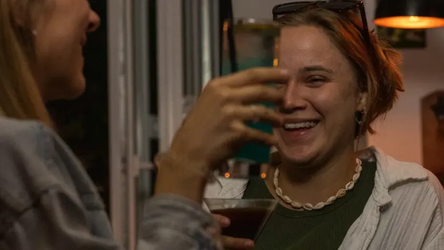 Two people laughing and holding drinks indoors.