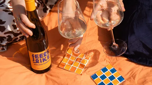 Hände halten Weingläser auf orangefarbener Decke.