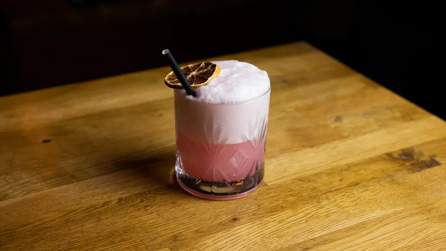 Pink cocktail with foam and dried citrus on table.