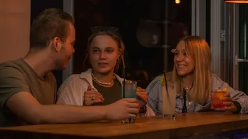 Three people sitting at a bar, drinking cocktails.