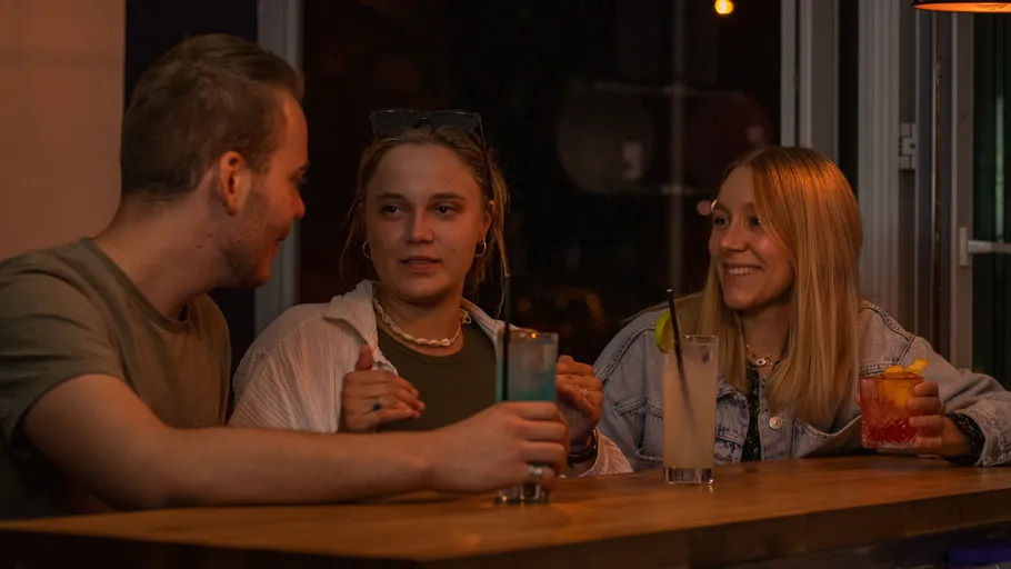 Three people sitting at a bar, drinking cocktails.