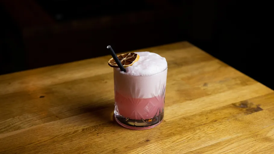 Pink cocktail with foam on wooden table.
